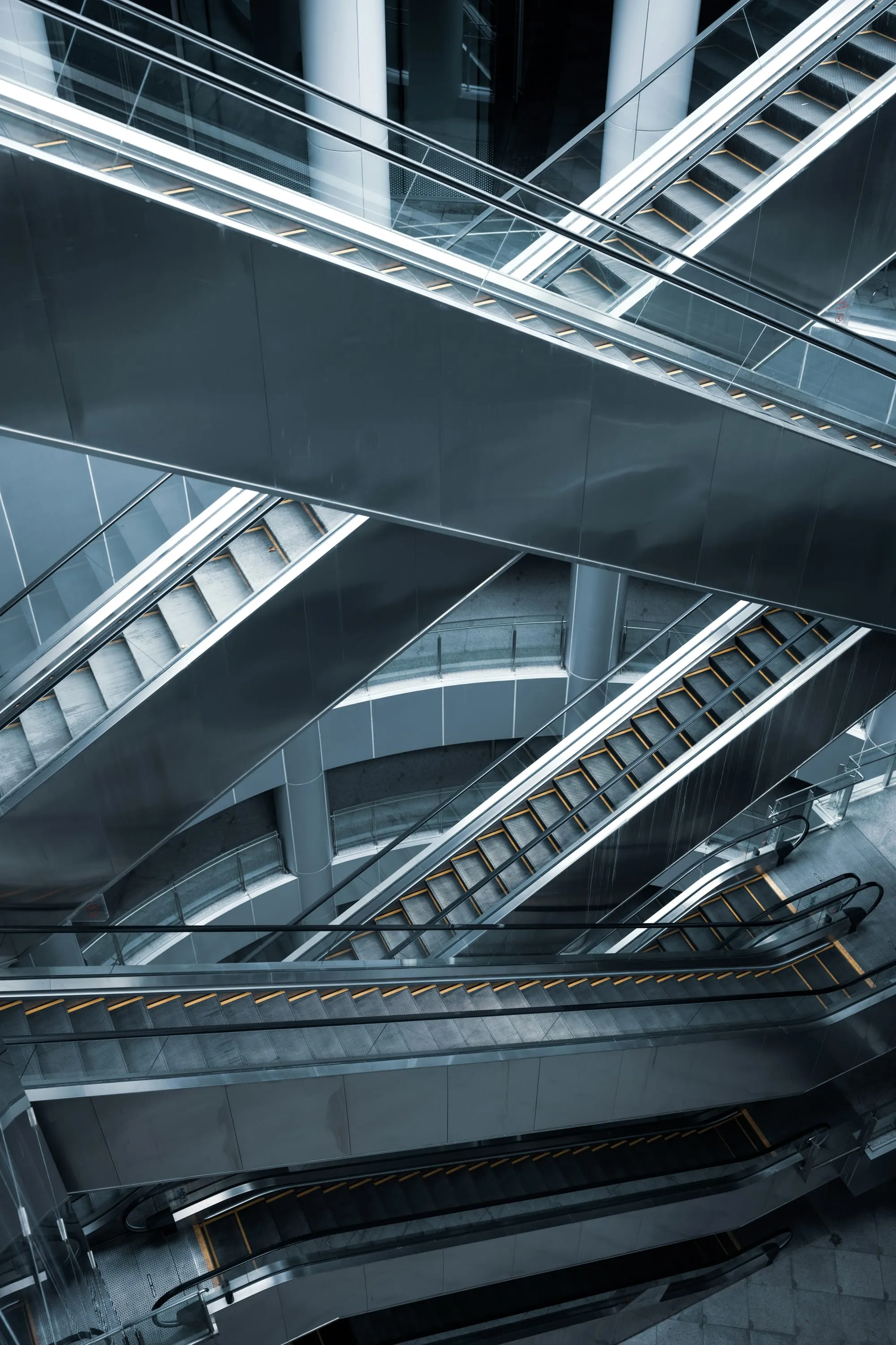 Mehrere sich kreuzende Rolltreppen aus Edelstahl und Glas in einem Gebäude, von oben gesehen